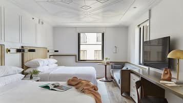 Ein Hotelzimmer mit zwei Betten, einem Schreibtisch, einem Fernseher und einem Fenster.