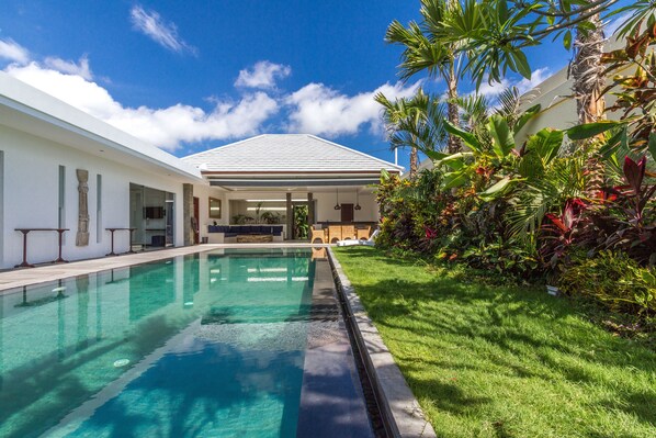 A modern house with a swimming pool, a covered patio, and lush tropical landscaping.