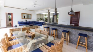 Amplia sala de estar con una mesa de comedor de vidrio rodeada de sillas de mimbre, un sofá azul y una pared de acento de piedra.