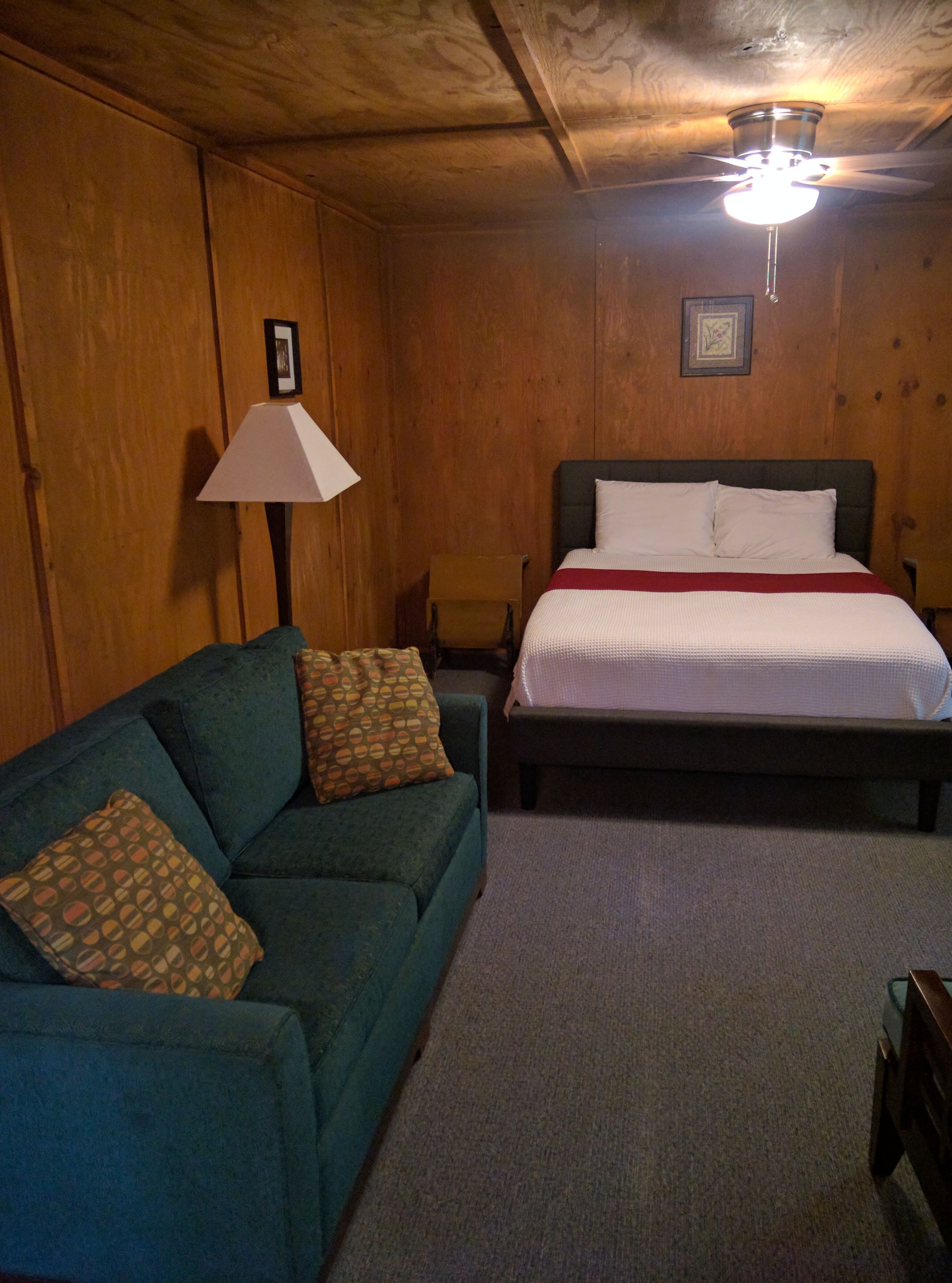 A bedroom with a bed, a green sofa, a lamp, and wooden walls.