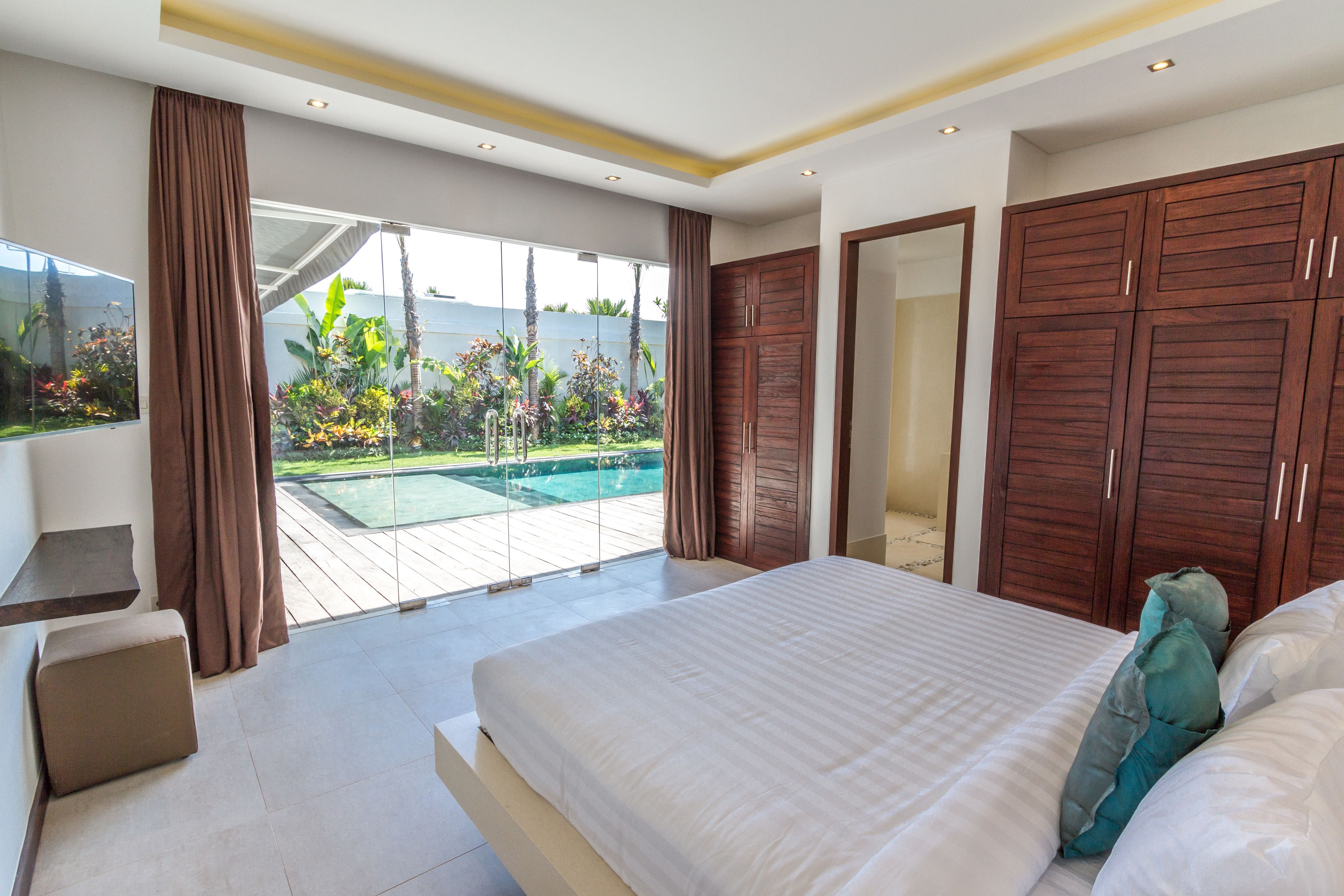 Un dormitorio con una cama grande, vistas a una piscina y armarios de madera.