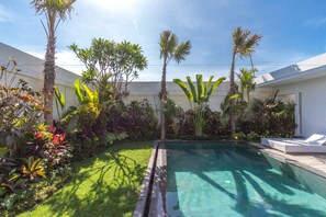 A swimming pool surrounded by lush tropical plants and a white building with a flat roof. - Villa Nala (Seminyak)
