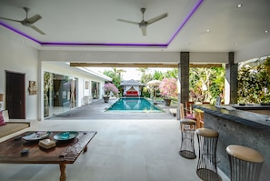A spacious indoor area with a pool, ceiling fans, and a bar area with stools. - Villa Nala (Seminyak)