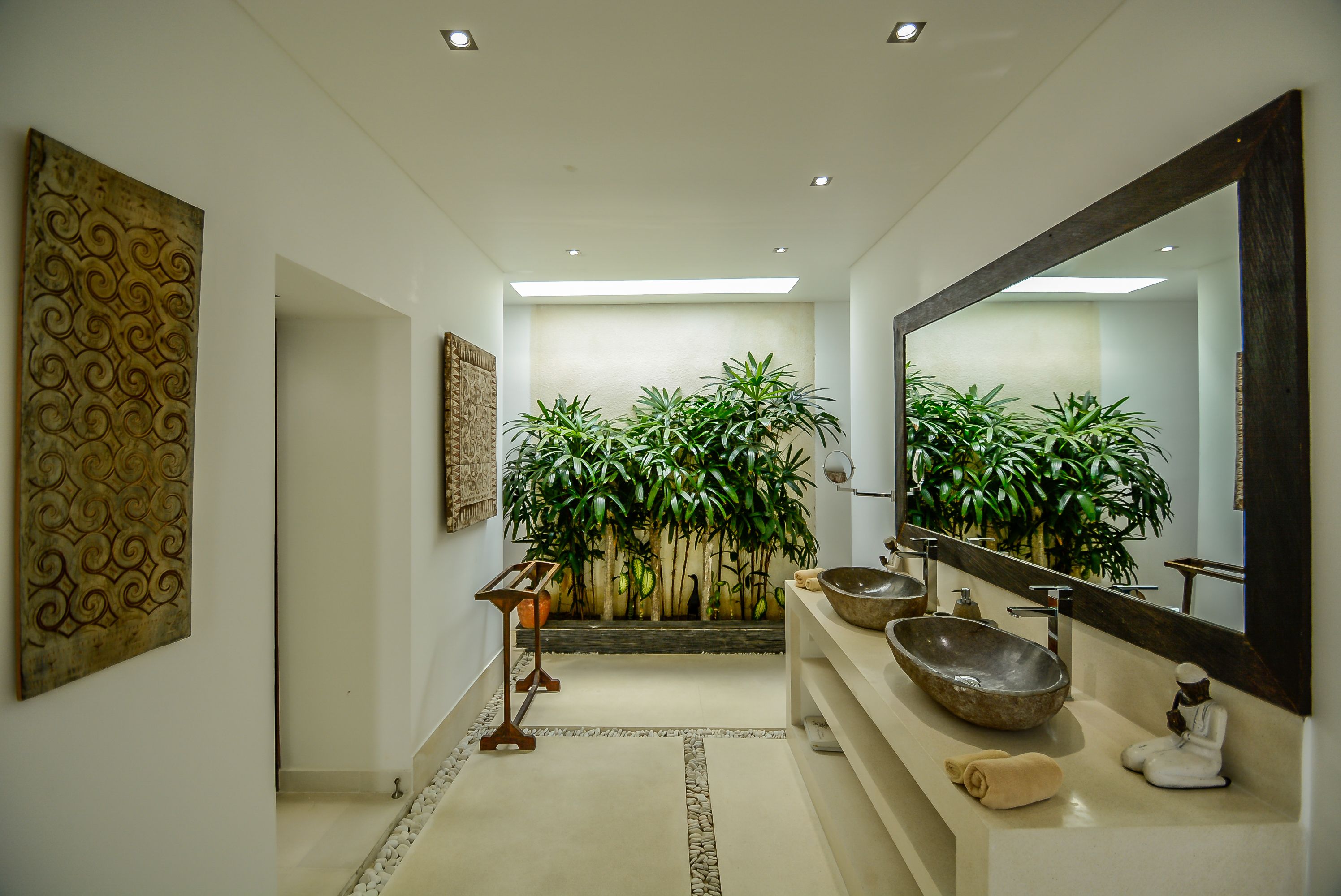 A modern bathroom with a large mirror, two sinks, and decorative plants.
