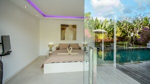 A modern bedroom with a large bed, a painting on the wall, and a TV on the left. The room has a glass door leading to a pool area with a view of lush greenery and a clear sky. - Villa Nala (Seminyak)