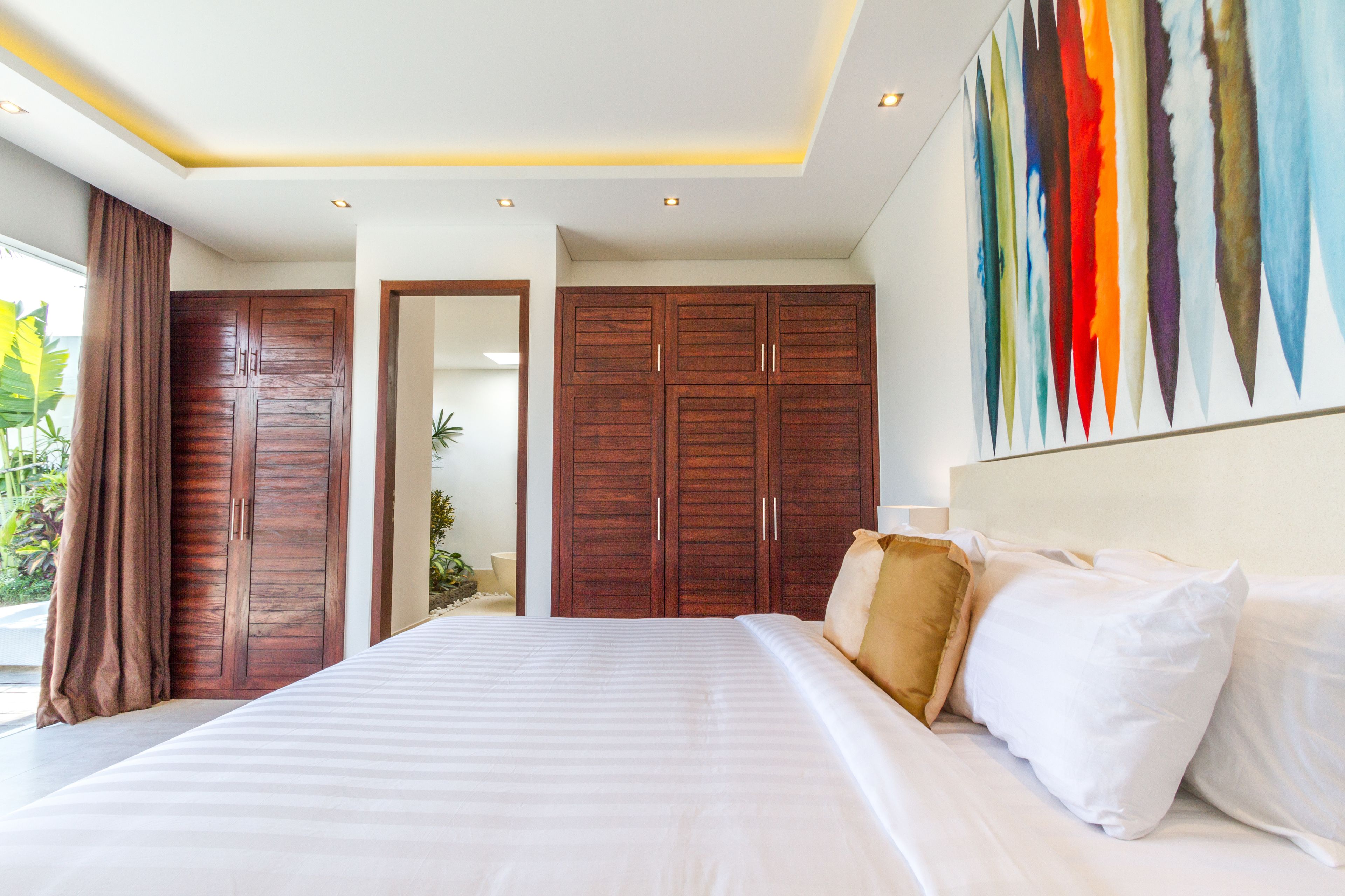 Un dormitorio moderno con una cama grande, armarios de madera y un cuadro abstracto colorido en la pared.