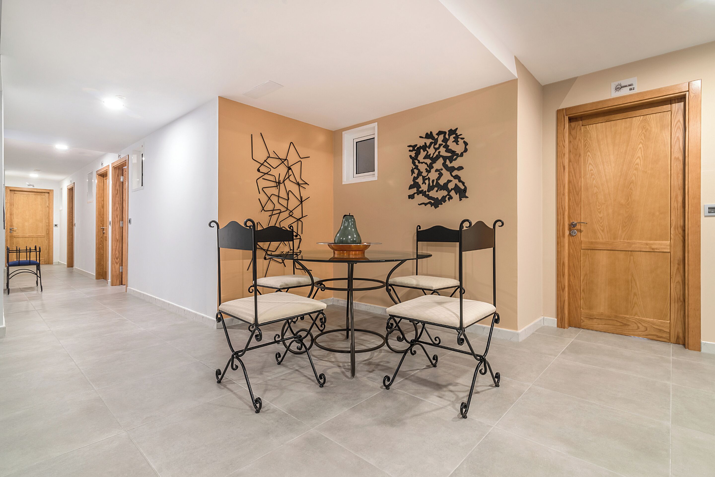 A dining area with a round table and four chairs, a decorative wall piece, and a door with a nameplate.