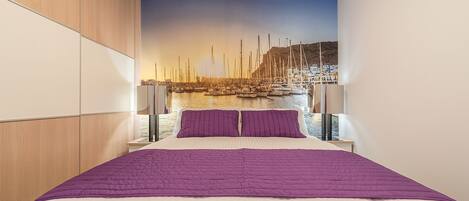 A bedroom with a large bed, a wooden wardrobe, and a mural of a marina.