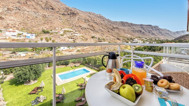 A balcony with a table set for breakfast, overlooking a pool and a mountainous landscape. - Sol Mogan Suites (Mogan)