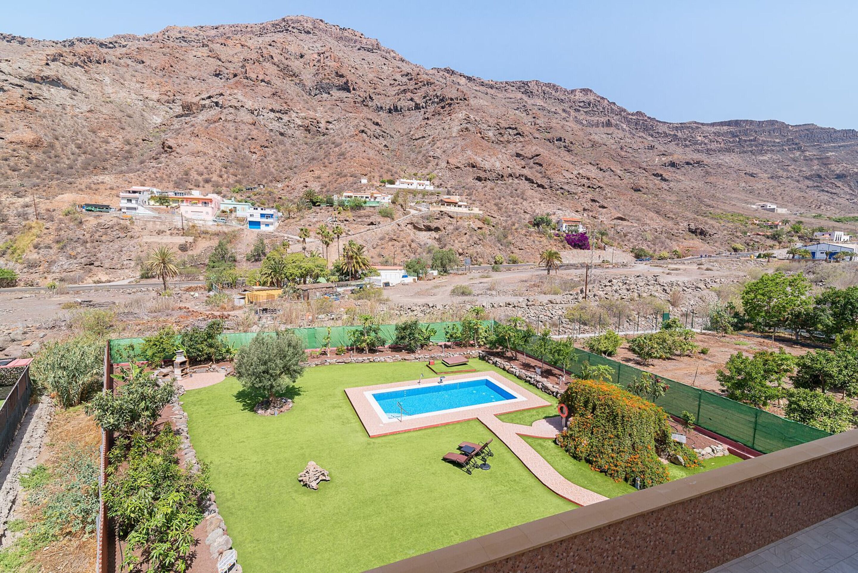 A residential area with a swimming pool, green lawn, and houses on a hillside.