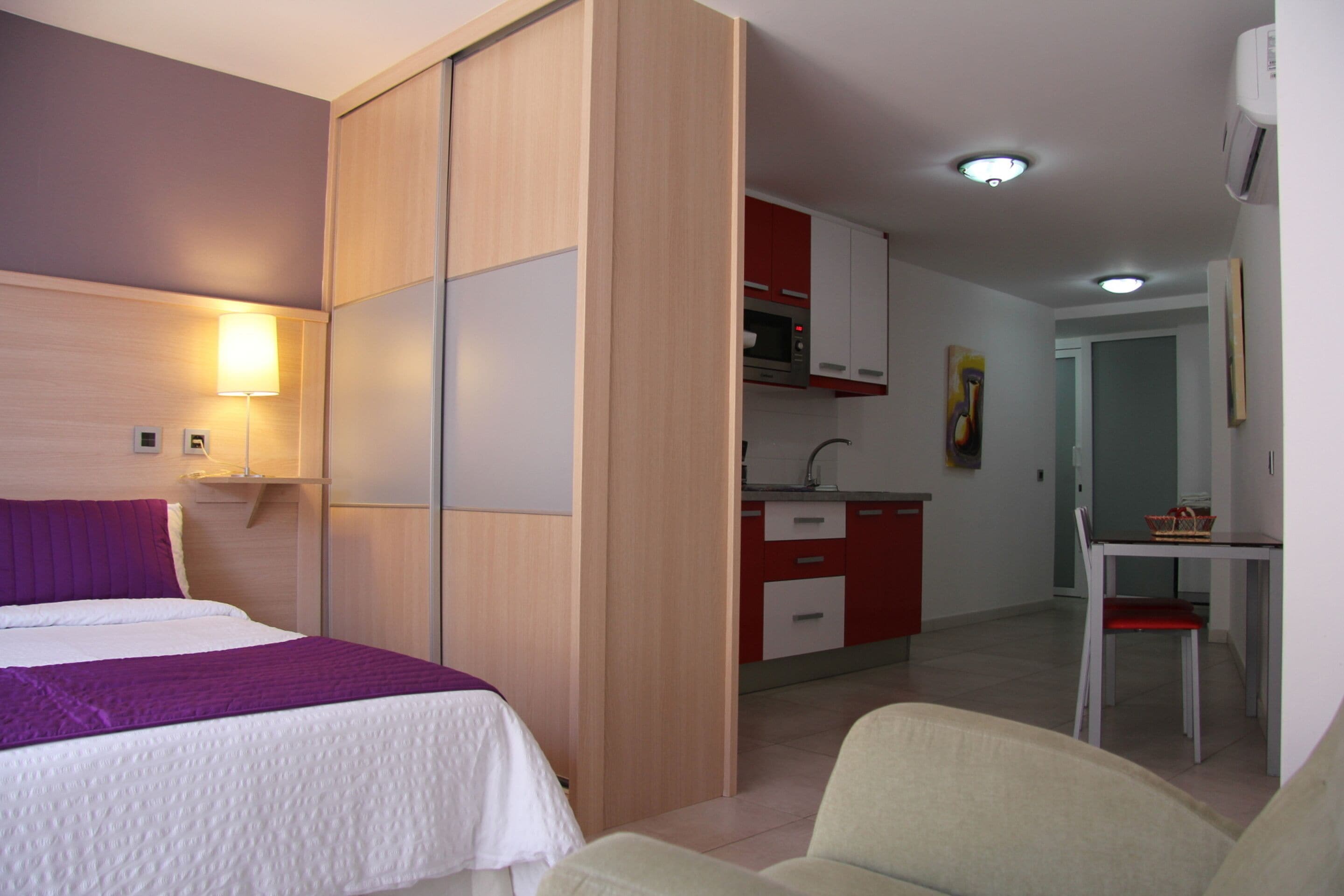 Hotellihuone, jossa on sänky, työpöytä, tuoli, pieni keittiö ja kylpyhuone.