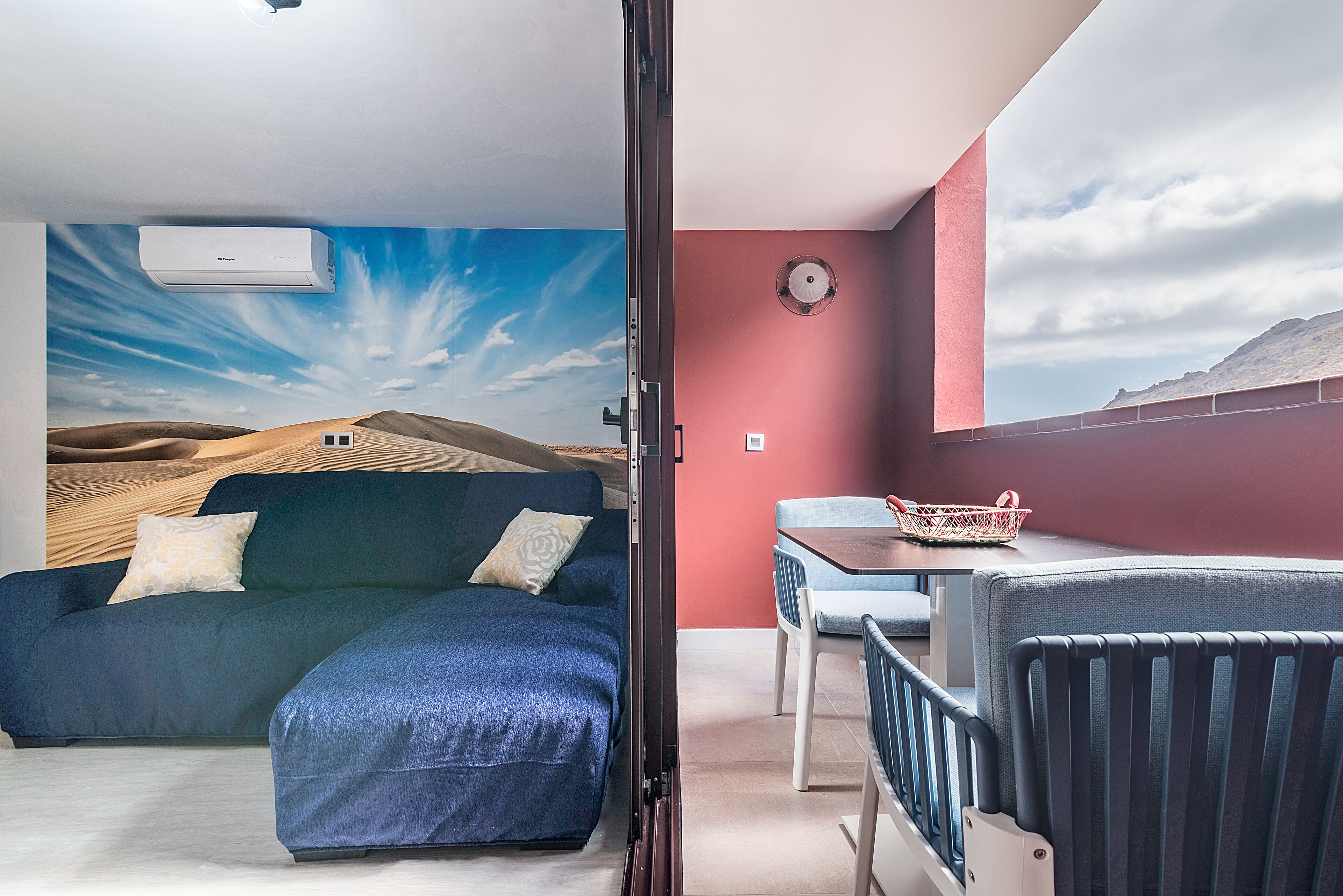 Una habitación con un sofá azul, una mesa de comedor y una pared roja.
