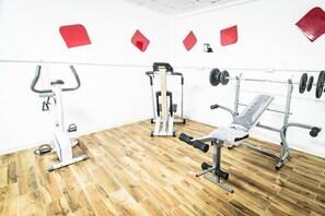 A gym with exercise equipment, including a stationary bike, a leg press machine, a bench press, and a squat rack with weights. - Sol Mogan Suites (Mogan)