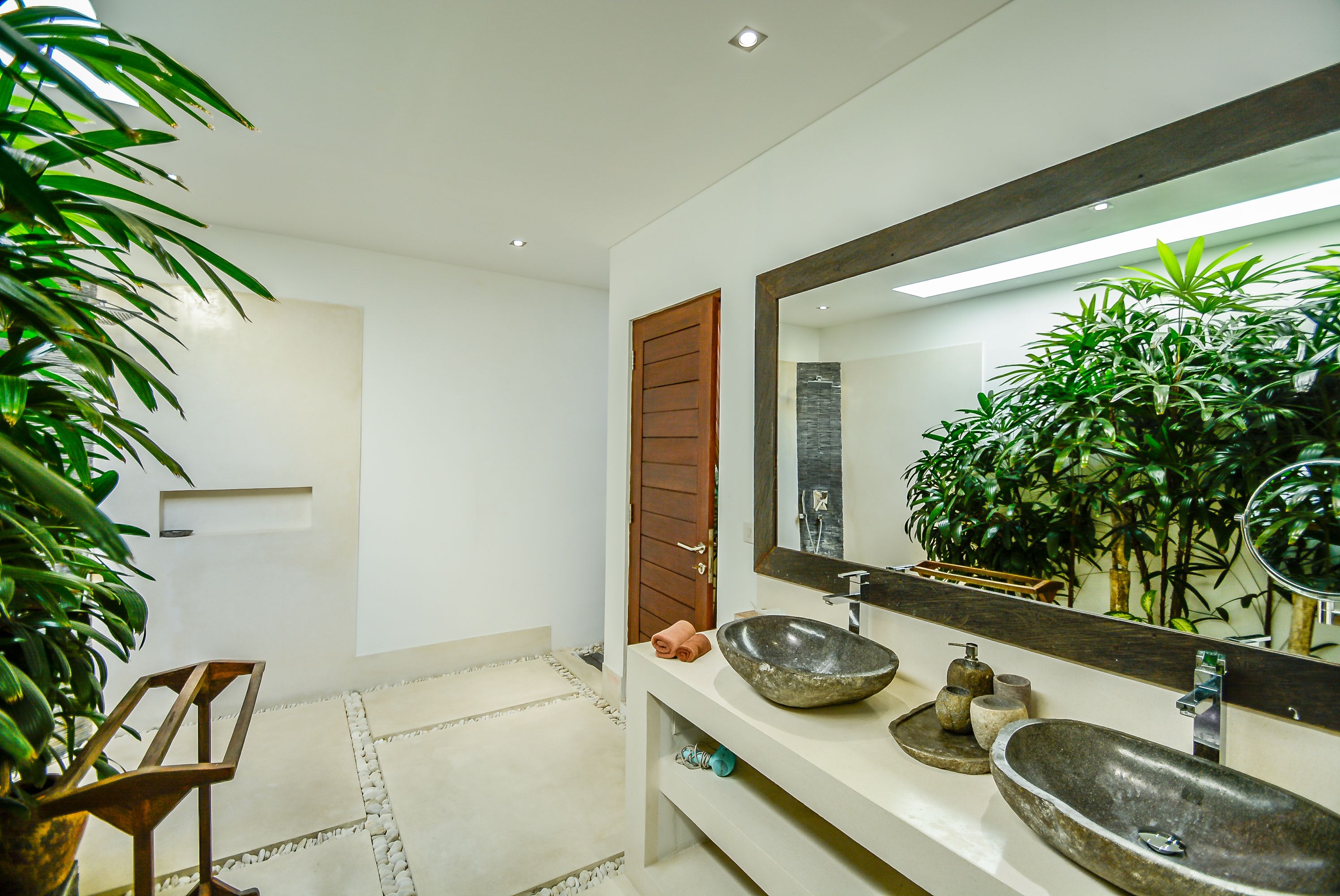 A modern bathroom with a large mirror, two vessel sinks, and a potted plant.