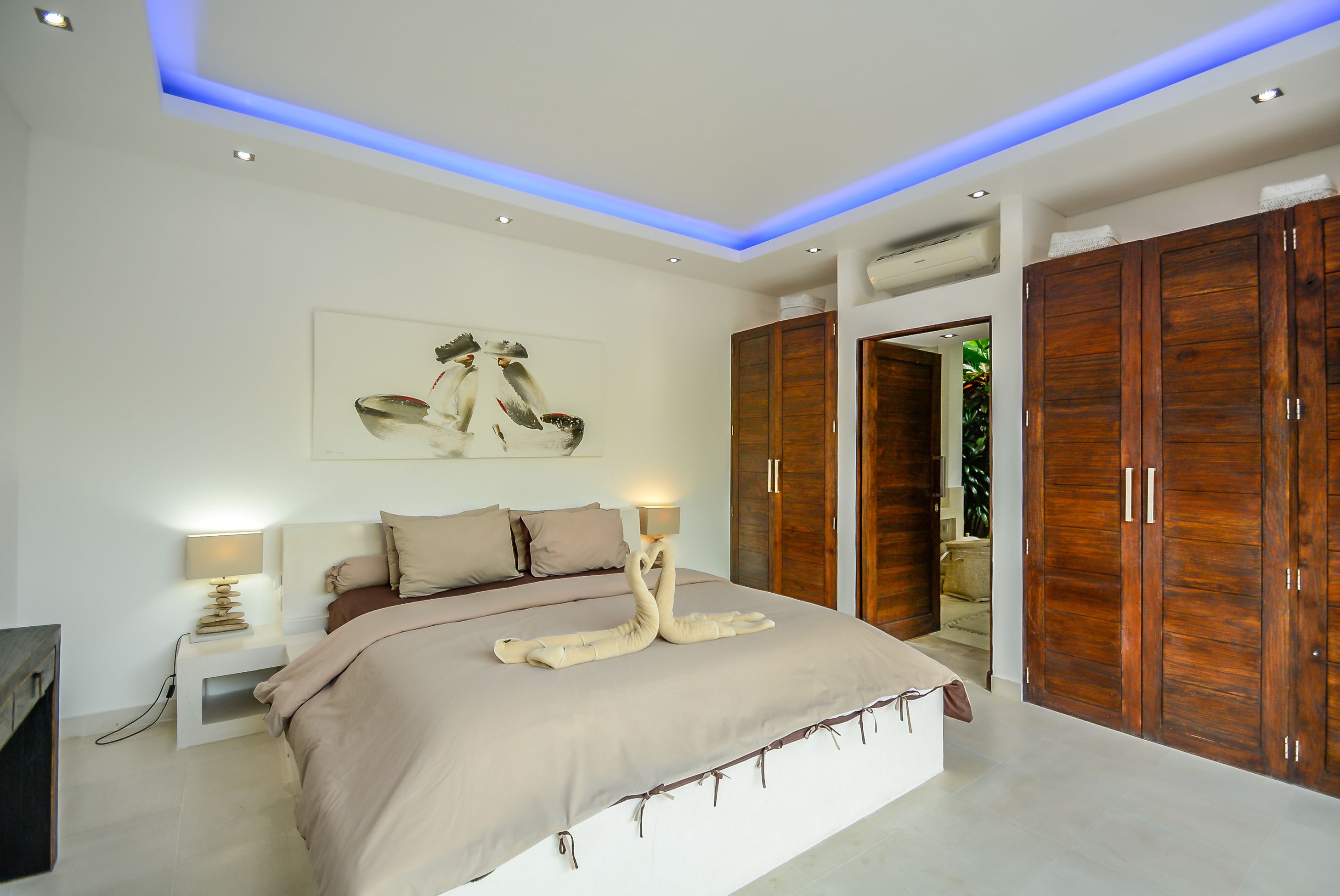 Een moderne slaapkamer met een groot bed, een houten garderobe en een plafond met blauwe verlichting.