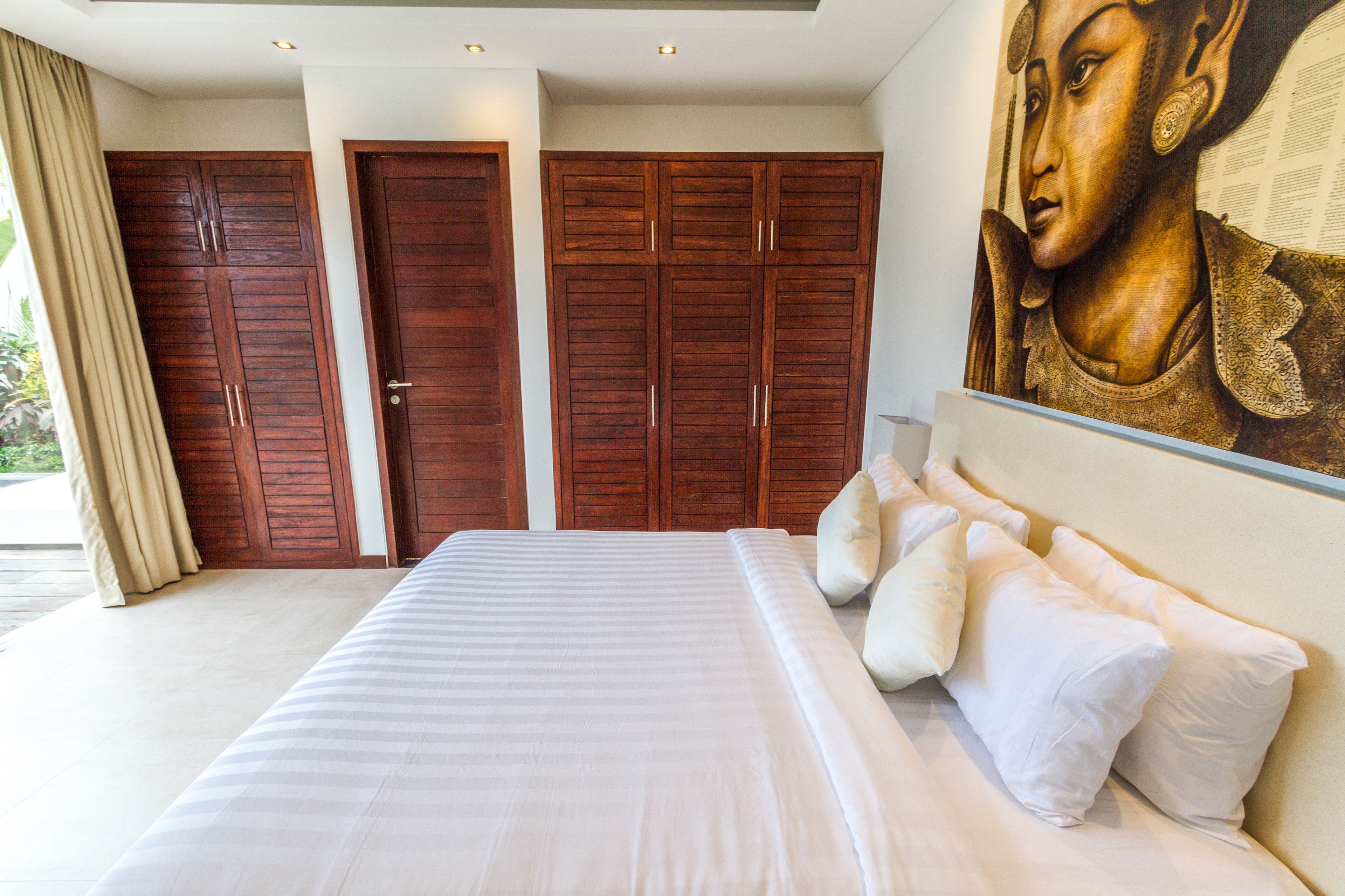 A bedroom with a large bed, wooden wardrobes, and a mural on the wall.