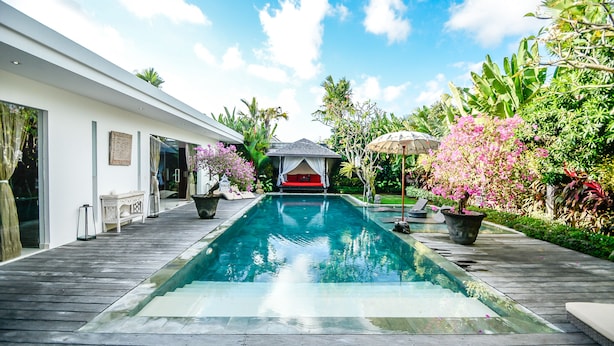 A modern pool area with a wooden deck, a red gazebo, and lush tropical plants. - Villa Saha (Seminyak)