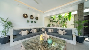 A modern living room with a sectional sofa, a glass coffee table, and decorative wall art. - Villa Tira (Seminyak)