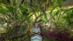 A Buddha statue surrounded by lush greenery and plants. - Villa Tira (Seminyak)