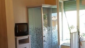 A bathroom with a shower, a television on a cabinet, and a chandelier. - Affittacamere Grandpa Mau (Lucca)