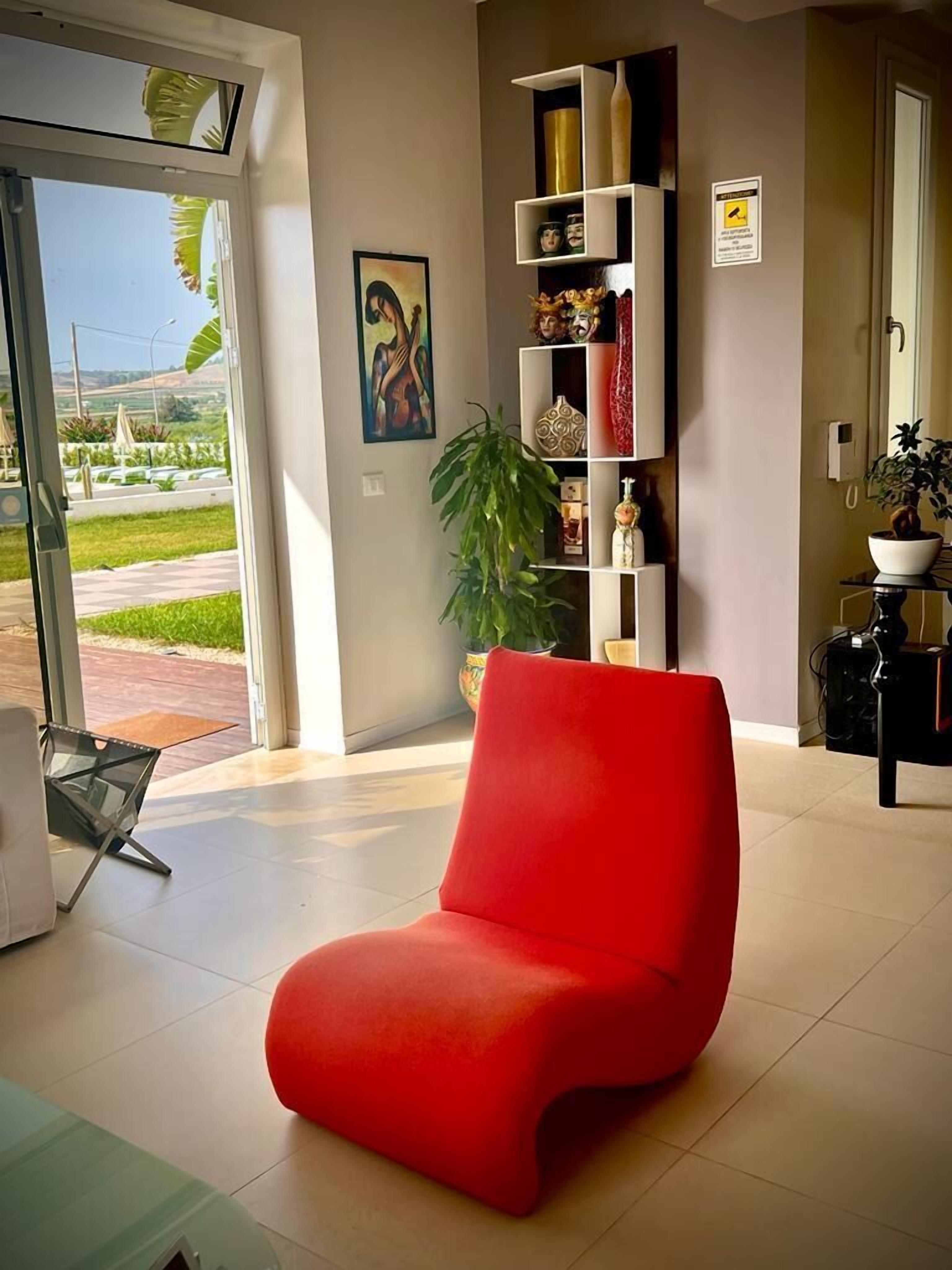 Una sala de estar moderna con un sillón rojo, una mesa de centro de vidrio, una planta en maceta y una estantería contra la pared.