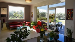 Un espace d’accueil moderne avec un canapé rouge, une table basse et un vase de fleurs. De grandes fenêtres offrent une vue sur l’extérieur.