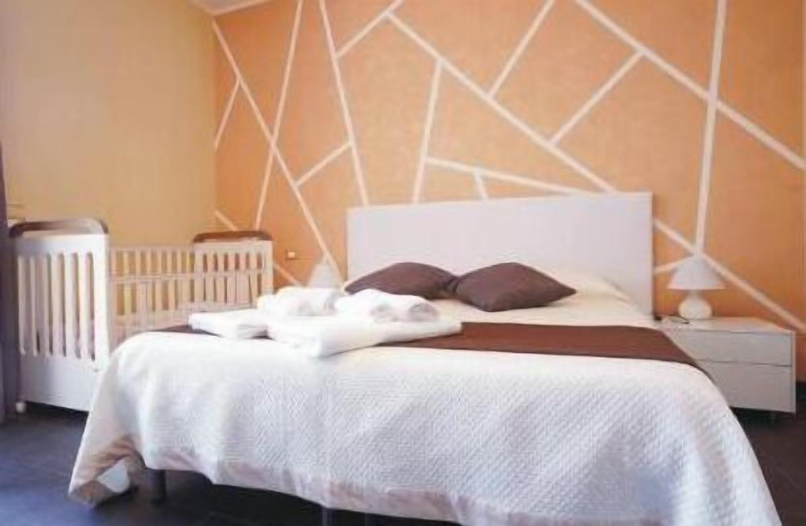 A neatly made bed with white linens and two dark pillows, a white bedside table with a lamp, and a radiator on the left.