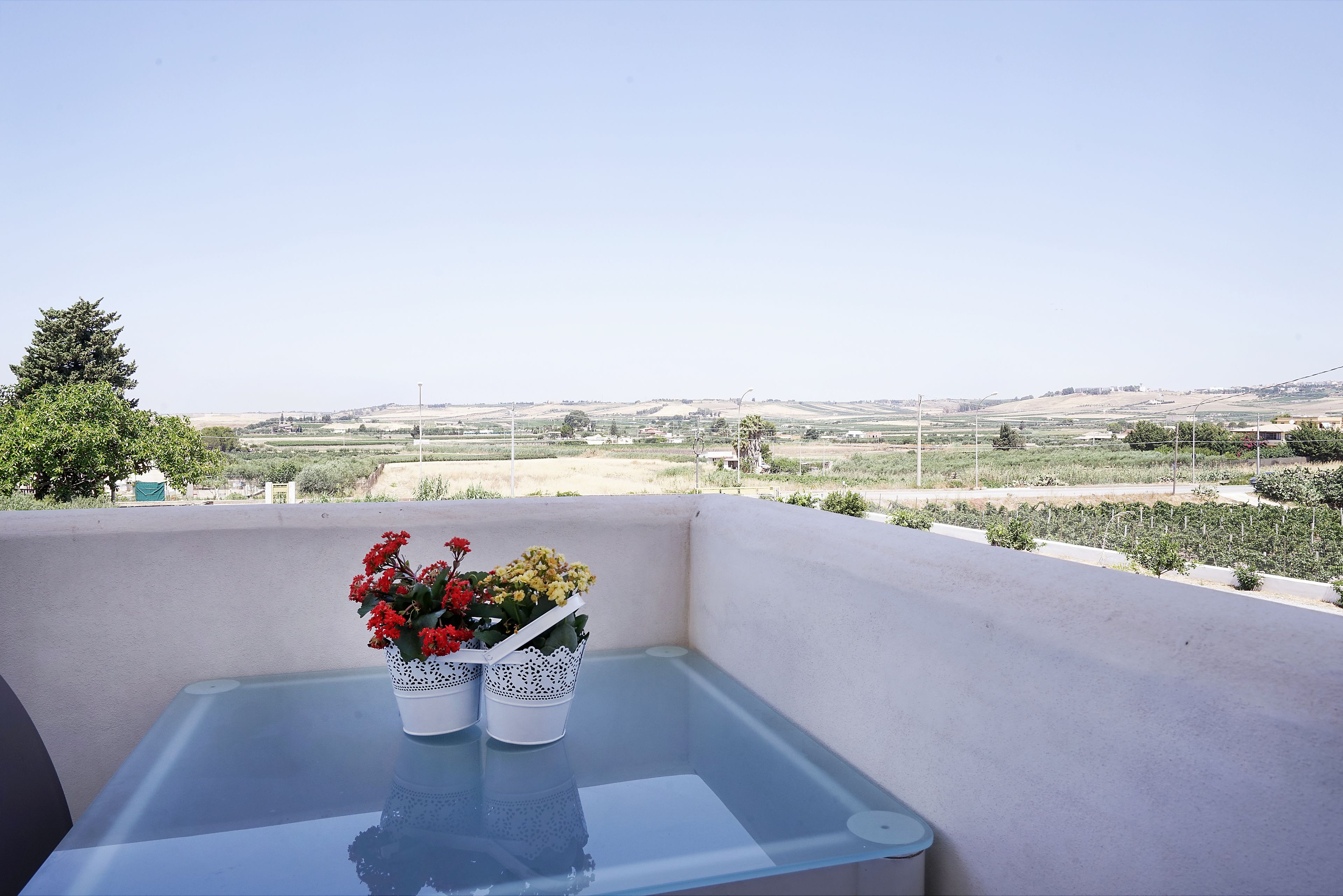 Ein Balkon mit einem Glastisch und zwei weißen Blumentöpfen mit Blumen.