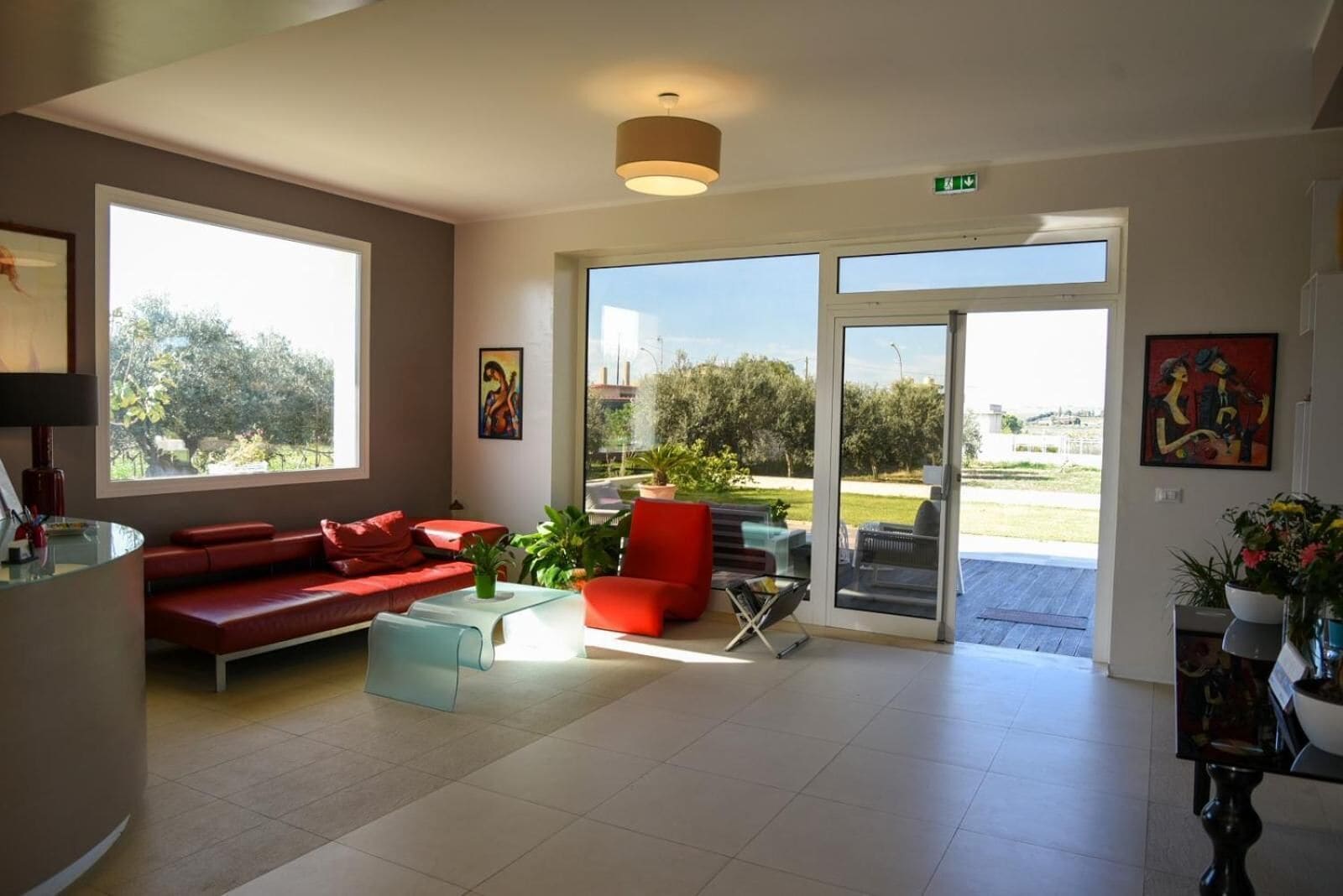 Un vestíbulo espacioso con un sofá rojo, una mesa de centro de vidrio y una lámpara moderna.