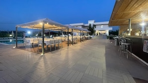 Un espace de restauration en plein air avec des tables et des chaises sous des auvents, une piscine et un bâtiment abritant un bar.
