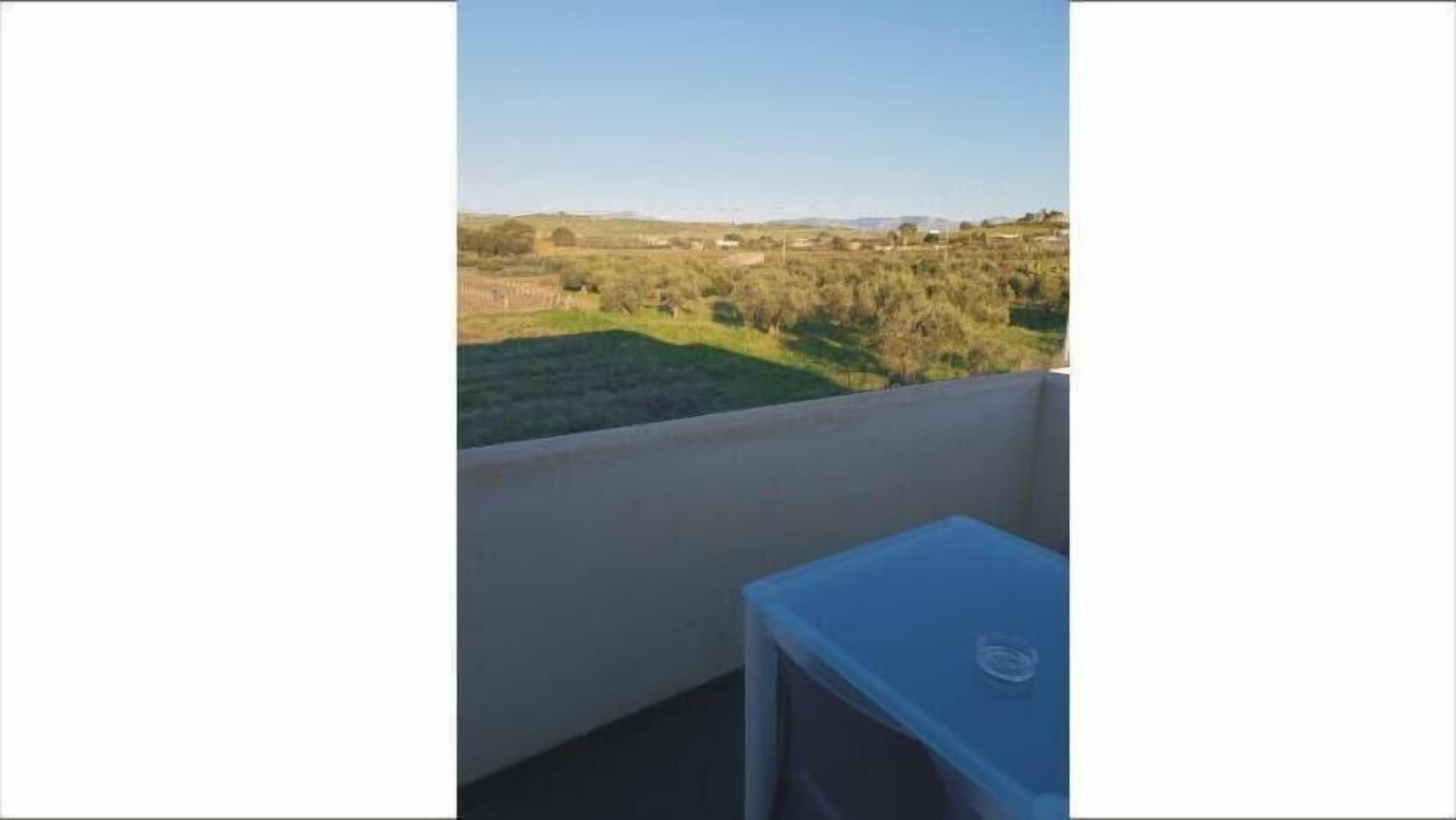 A balcony with a view of a grassy field and distant hills.