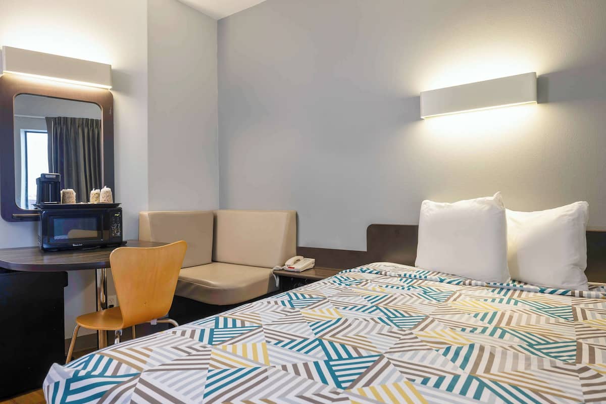 Hotelkamer met een bed, een bureau met stoel, een magnetron, een telefoon en een spiegel.