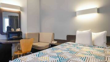 A hotel room with a bed, a desk with a chair, a microwave, a telephone, and a mirror.
