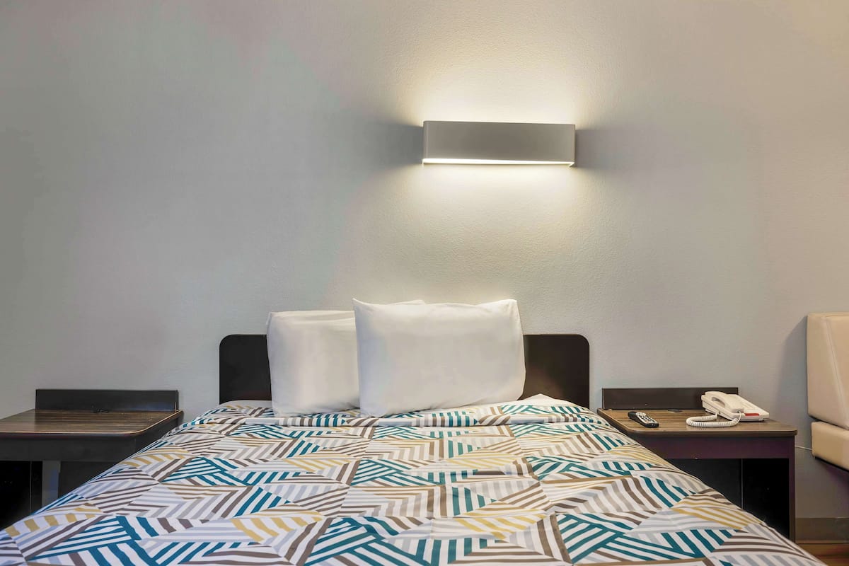 Een hotelkamer met een bed, twee nachtkastjes, een bedlamp, een telefoon en een wandlamp.