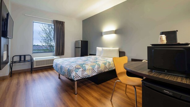 Quarto de hotel com cama, escrivaninha, cadeira, televisão e janela com cortinas.