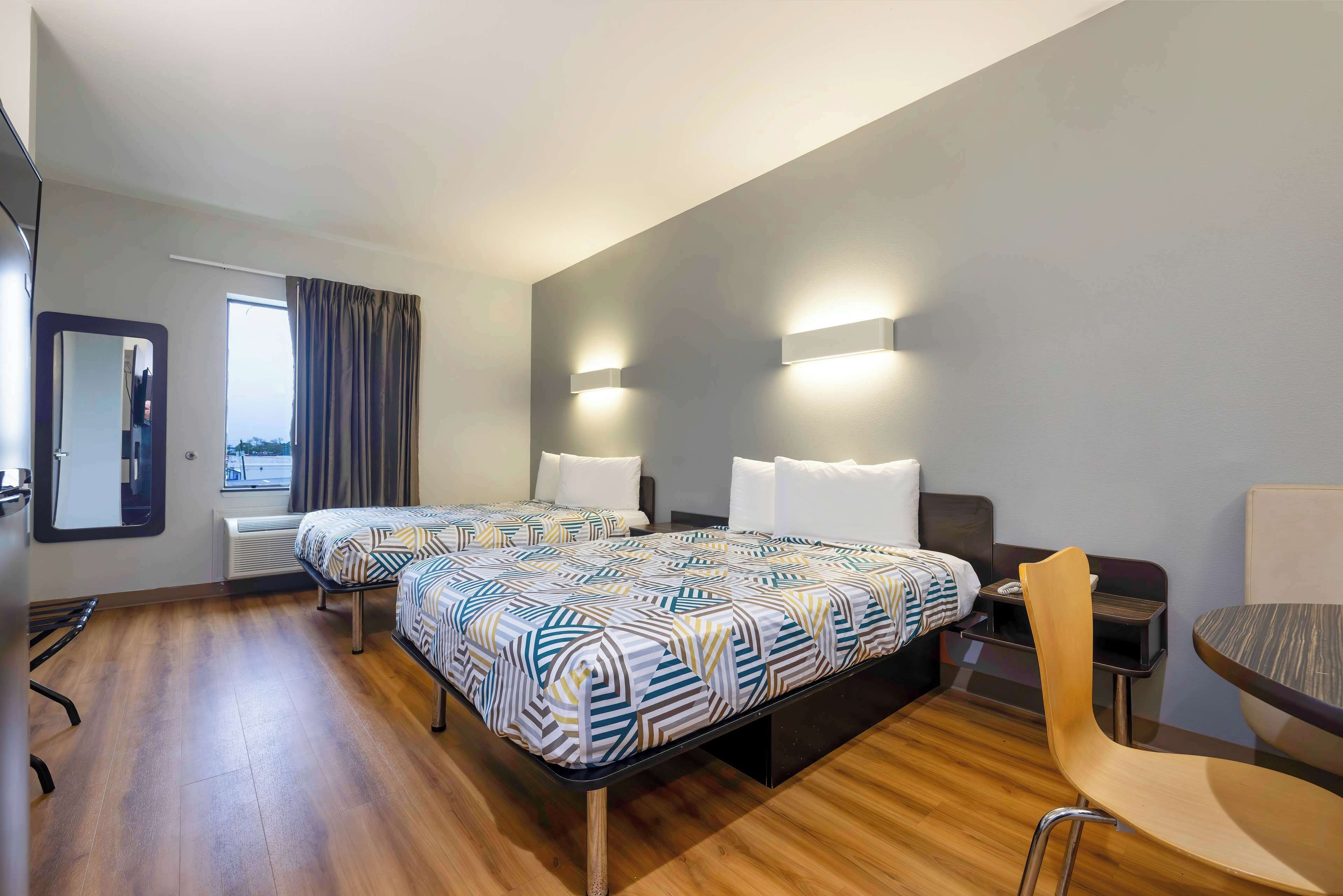 Une chambre d’hôtel avec deux lits, un bureau, une chaise et une fenêtre avec des rideaux.