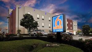 Edifício do 6 Motel & Studio, com um grande letreiro de entrada, estacionamento e áreas verdes ao redor.