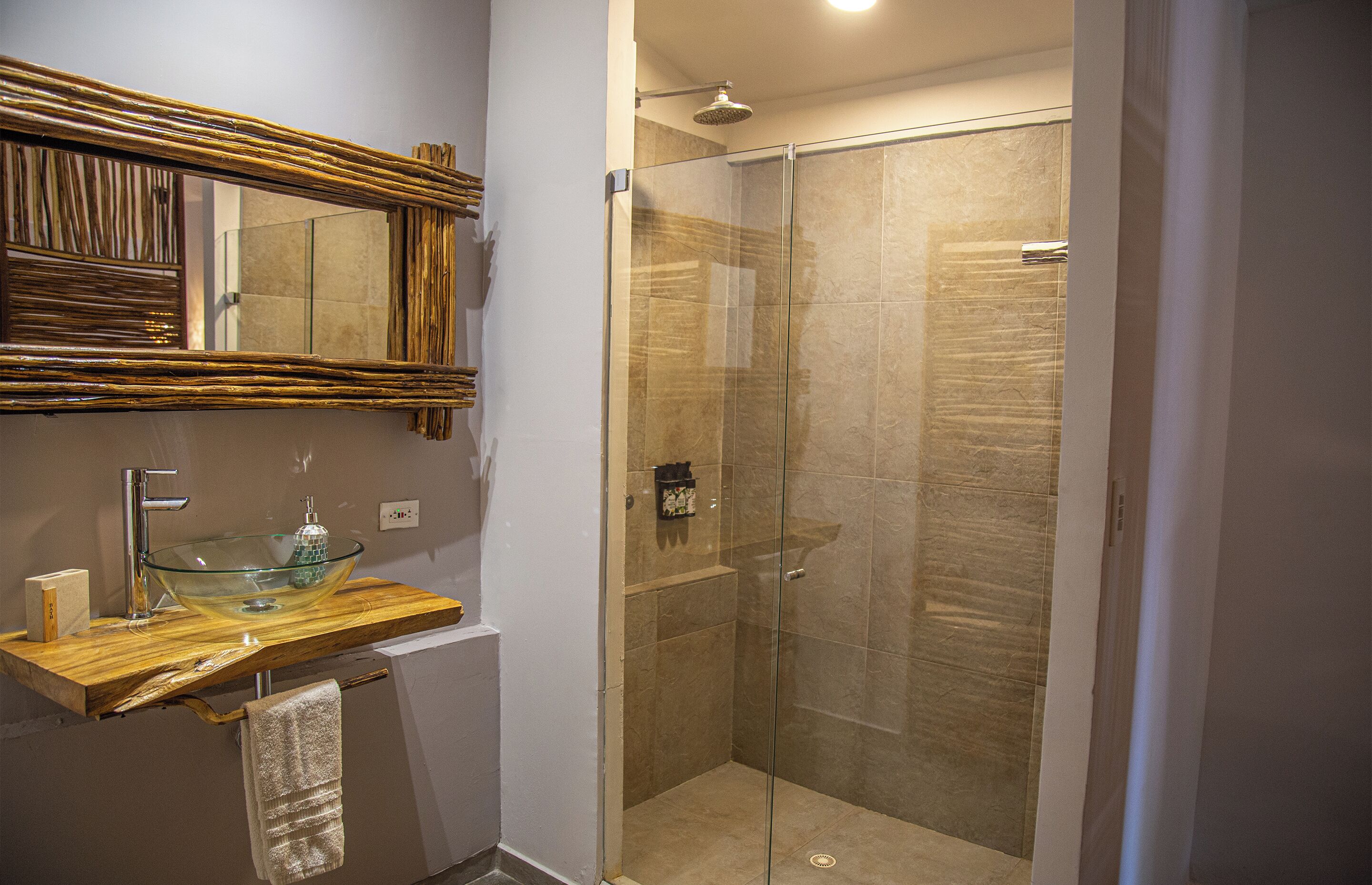 A bathroom with a glass-enclosed shower, a wooden vanity with a glass bowl sink, and a large mirror.