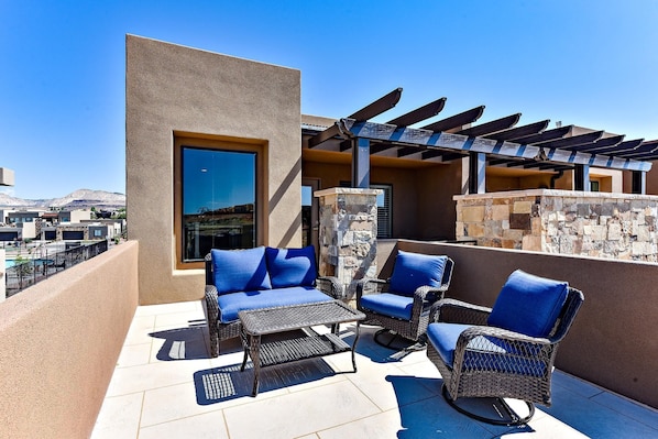 A rooftop patio with wicker furniture, a pergola, and a view of the surrounding landscape.