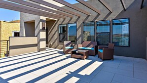 An outdoor patio area with a modern architectural design, featuring a pergola structure, two wicker sofas with blue cushions, and a small table. - Greenwind (St. George)