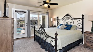 A bedroom with a bed, a ceiling fan, a nightstand, and a view of a swimming pool through a glass door. - Greenwind (St. George)