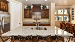 A kitchen with a granite countertop, stainless steel refrigerator, wooden cabinets, and a 'WELCOME' sign above the sink. - Greenwind (St. George)