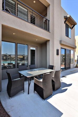 A patio with a table and chairs, a pool in the background, and a building with a balcony. - Greenwind (St. George)