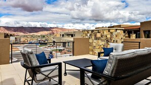 A balcony with wicker furniture, a stone wall, and a view of a desert landscape. - Snow Canyon Sunrise (St. George)