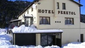 Ein zweigeschossiges Gebäude mit der Aufschrift "HOTEL PERETOL", dessen Dach mit Schnee bedeckt ist und das an eine kleine Struktur angebaut ist.