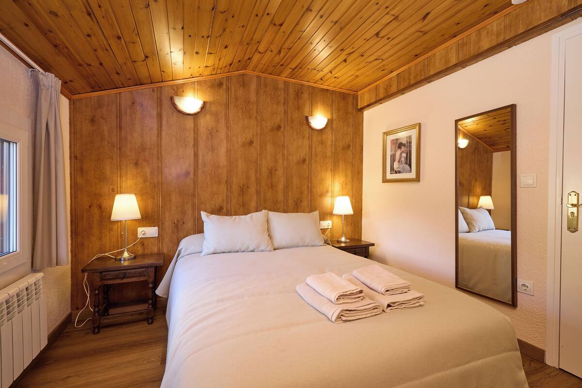 Ein Hotelzimmer mit Holzboden, zwei Nachttische mit Lampen, ein großes Bett mit weißer Bettwäsche, ein Spiegel und ein gerahmtes Bild an der Wand.