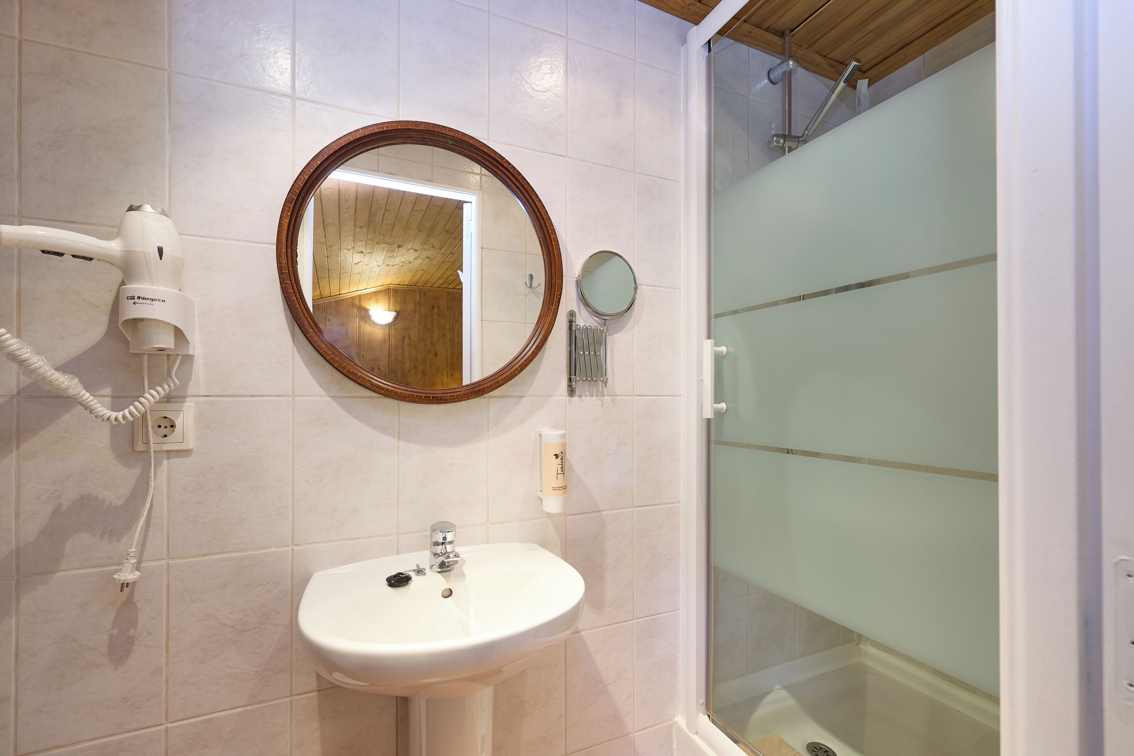 A bathroom with a sink, a hairdryer, a mirror, and a shower.