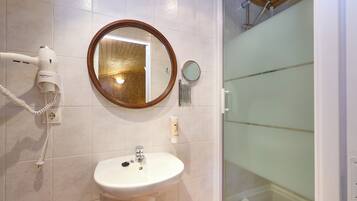 A bathroom with a sink, a hairdryer, a mirror, and a shower.