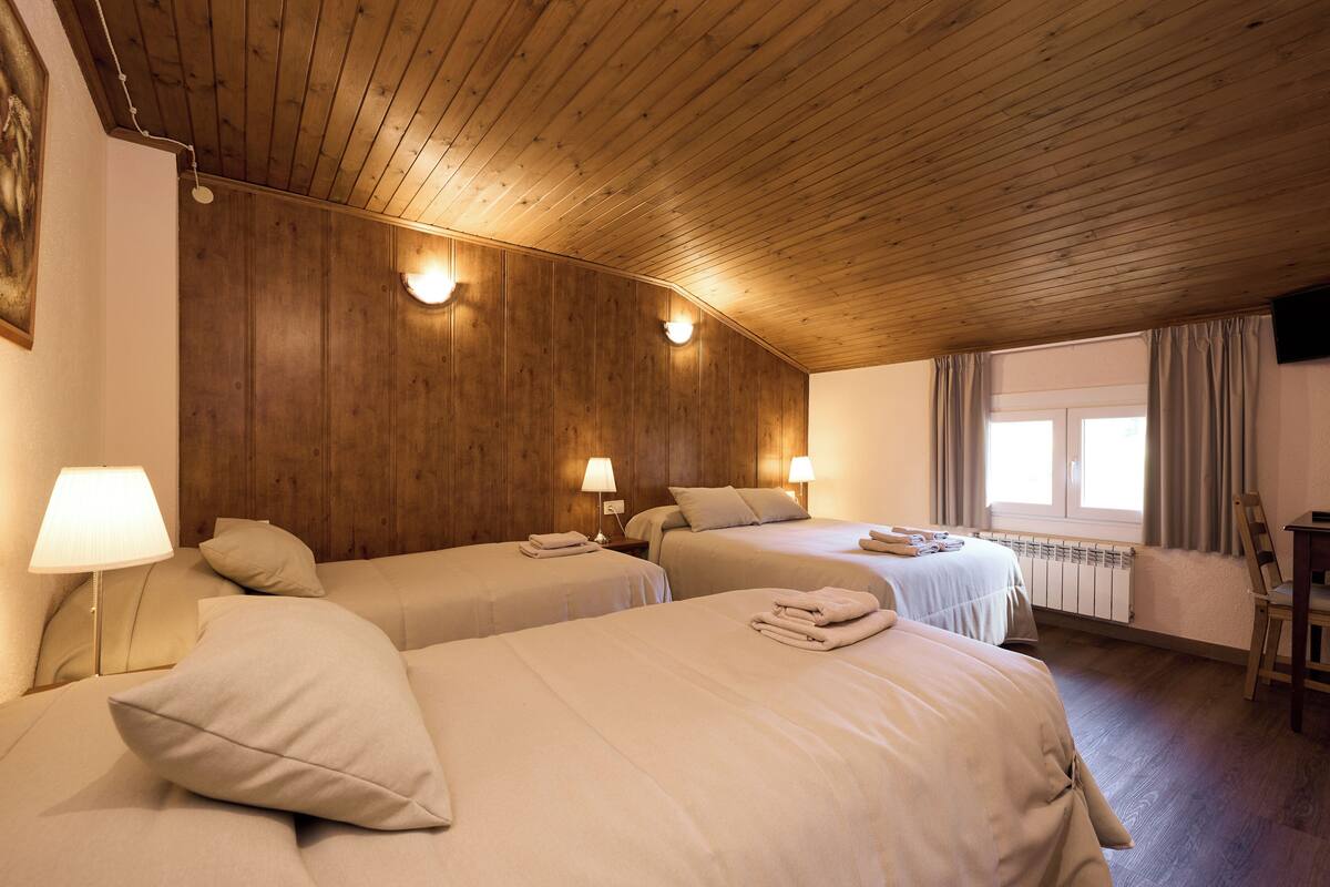 Ein Hotelzimmer mit Holzboden, zwei Betten mit beige farbenen Bettwaren, Nachttischlampen, einem Fenster mit Vorhängen und einem Heizkörper.