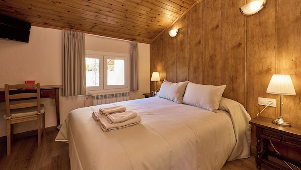 Ein Schlafzimmer mit Holzboden, einem Bett mit weißen Leinentüchern, zwei Nachttischlampen, einem Holzstuhl und einem Fenster mit Vorhängen.